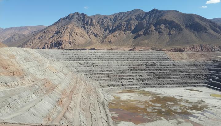 Огромное террасное хвостохранилище медного рудника на фоне скалистого горного пейзажа в Андах, Чили.
