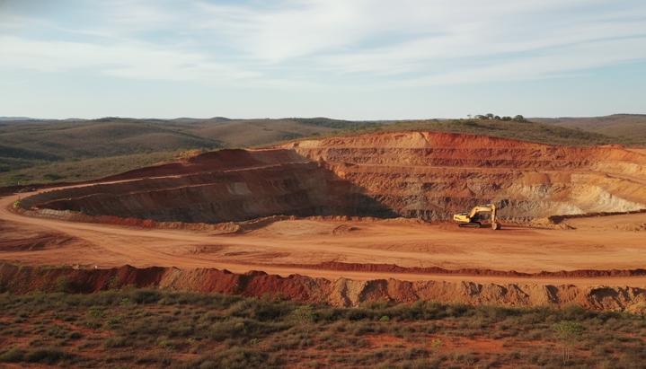 Карьер по добыче редкоземельных металлов в Бразилии. Видны холмы, красно-оранжевая глина и одинокий экскаватор.